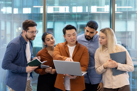 A diverse team collaborates around a laptop in a modern office setting, brainstorming ideas and...