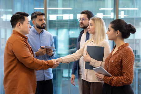 Diverse business team shaking hands in modern office setting, symbolizing partnership and...