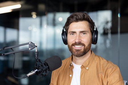 A cheerful podcaster wearing headphones is seated in a modern studio environment with glass walls....