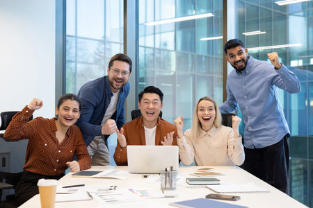 An enthusiastic team of diverse coworkers cheerfully celebrates success during a collaborative...