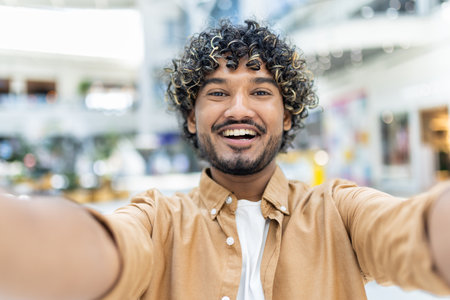 A joyful young man smiling confidently while taking a selfie in a contemporary indoor setting, showcasing happiness and self-confidence.の写真素材