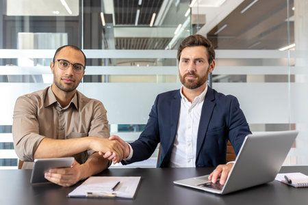 Business professionals sitting in an office setting, shaking hands to finalize a collaboration. They...