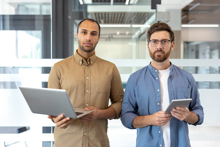 Dynamic collaboration of two professionals standing in a modern office, showcasing teamwork and...