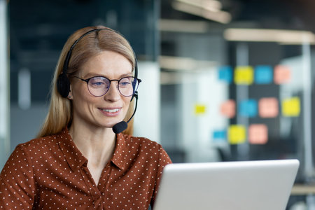 A confident businesswoman in glasses and headset reviewing tasks on a laptop, collaborating...