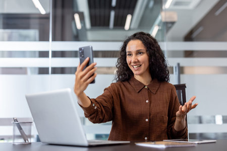 Woman in a professional work setting engaged in a cheerful conversation via a smartphone.