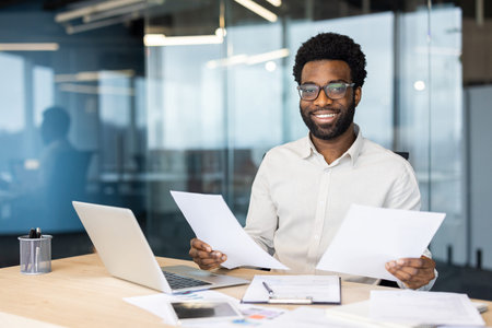 A confident businessman reviews documents at his desk, smiling in a modern office environment. The scene evokes professionalism, success, and determination, showcasing a positive attitudeの写真素材