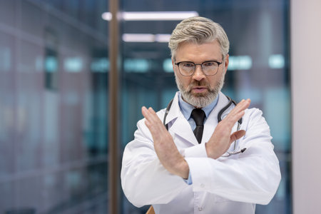 Experienced male doctor making a hand gesture, showing a critical warning inside a medical facility.の写真素材