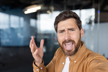 Stressed businessman shouting during a video call in the office, conveying deep frustration and anger stemming from overwhelming work-related challenges and pressures.の写真素材