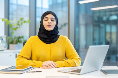 Young businesswoman wearing a hijab practicing mindfulness and taking a deep breath during her...