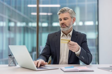 Businessman using laptop computer and holding a credit card, processing an online payment or...