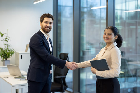 Business professionals sealing a deal with a firm handshake in a modern office, symbolizing...