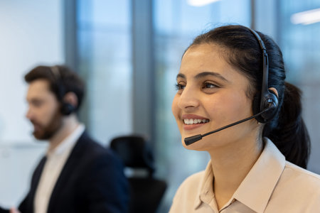 Female customer service representative smiling and talking on a headset while working in a busy call...