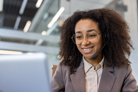 Close-up photo of a smiling young African-American businesswoman in a headset working in the office...