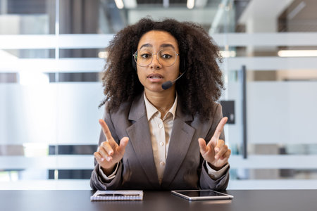 Portrait of a young African-American woman in a headset and suit sitting in the office at the table...
