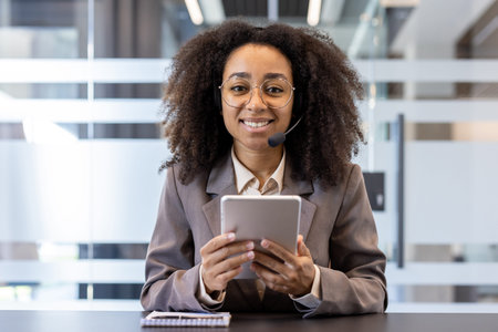 Portrait of a smiling young African American woman in a suit and headset, smiling at the camera,...