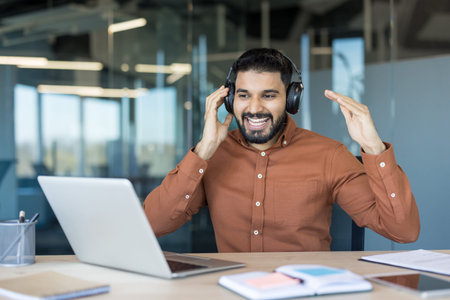 Happy young man wearing headphones, talking and gesturing during an online video conference or...