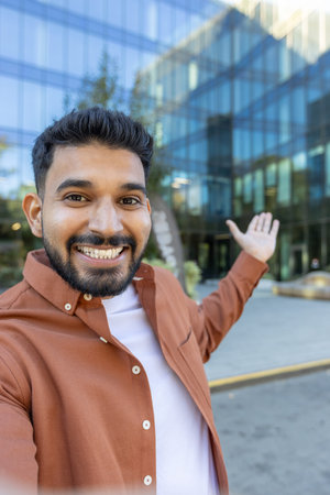 Young man smiling at camera, making a selfie video for social media and pointing to a contemporary...