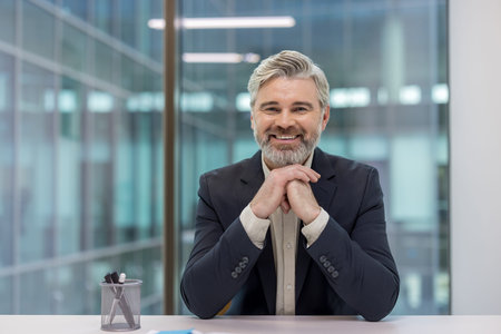 Accomplished senior businessman with gray hair and beard confidently smiling, projecting...