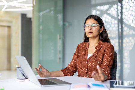 Office worker engaging in mindfulness meditation at her desk, enhancing mental wellness and promoting stress reduction while fostering a calm and focused work environmentの写真素材