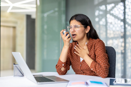 Young woman having a sudden asthma attack and breathing difficulty, using an inhaler to alleviate...