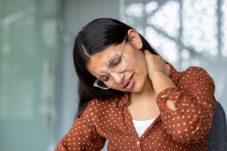 Young businesswoman suffering from neck pain, touching and massaging her painful neck with hand, tired from computer work, feeling exhausted, suffering from office syndromeの写真素材