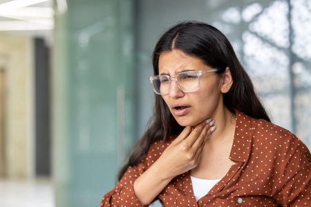 Young businesswoman wearing eyeglasses touching her neck, experiencing discomfort and difficulty...