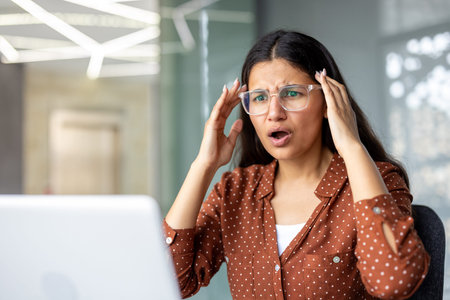 Woman in glasses holding temples, mouth open in disbelief, having a headache from unexpected bad...