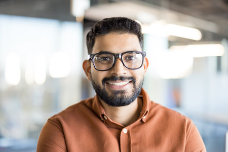Young indian man with a beard and glasses smiling confidently at the camera, portraying a successful...