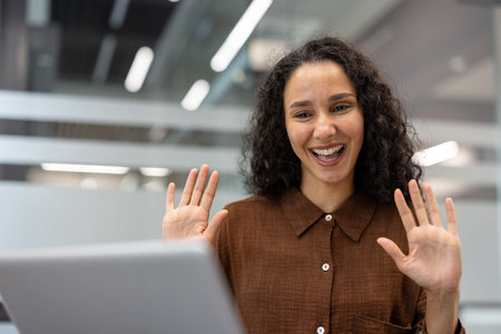 Woman engaging in a video call and happily waving her hands, communicating and participating in an...