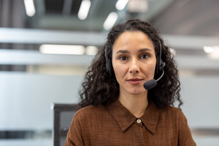 Woman with dark curly hair wearing a headset with a microphone, providing online customer support or...