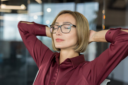 Businesswoman taking a mindful break, meditating to relieve stress, relaxing in an office chair with closed eyes and hands behind head, finding peace during a busy dayの写真素材
