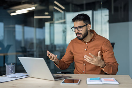 Male professional gesturing and explaining business concepts during a video call on laptop in a modern office, conducting a virtual meeting, training or presentation for remote teamの写真素材