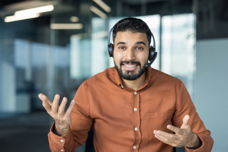 Young man wearing a headset and smiling, offering customer service assistance or participating in an online meeting, communicating with clients virtually from an officeの写真素材