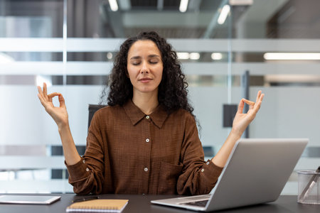 Professional businesswoman meditating at her office desk, practicing stress relief and mindfulness during a work break, finding inner peace and promoting mental wellnessの写真素材