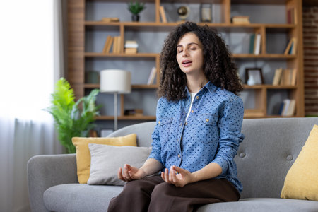 Young woman practicing mindfulness. Finding inner peace and enjoying tranquility while meditating on a comfortable sofa in her modern. Stylish living room. Creating a calming and relaxing atmosphereの写真素材