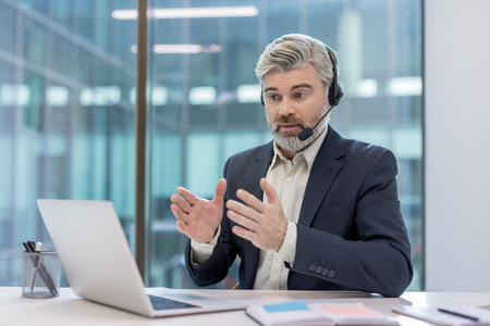 Businessman having a virtual meeting, communicating with clients or colleagues while working remotely from a modern office, providing support and actively discussingの写真素材