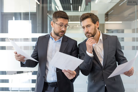 Two businessmen are collaborating while reviewing documents, analyzing important financial records...