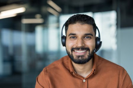 Young indian customer service agent with headset smiling confidently in modern office, providing friendly phone and online support as a professional call center representativeの写真素材