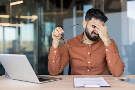 Young man feeling tired and having a painful headache, rubbing his temples in discomfort while...