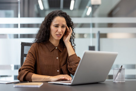 Woman experiencing a severe headache and high levels of stress while working on her laptop at an office desk, illustrating concepts of burnout and professional pressureの写真素材