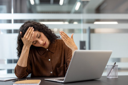 Young woman working from home experiencing a severe headache and burnout, feeling overwhelmed and frustrated by her workの写真素材