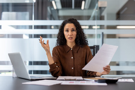 Businesswoman feeling stressed and overwhelmed, sitting at her office desk with laptop and...