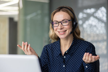 Friendly woman wearing a headset and glasses, actively engaging in a video call and discussing...