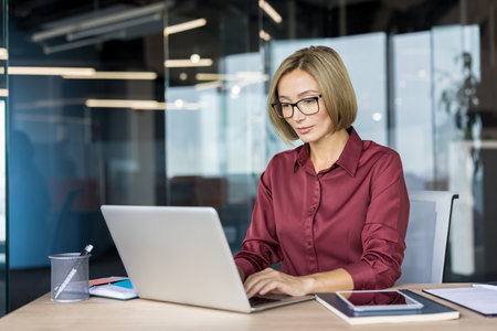Professional businesswoman concentrating on her work, typing on a laptop at a desk in a modern office, depicting dedication and productivity in a corporate environmentの写真素材
