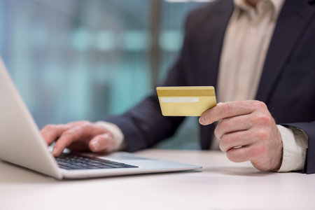 Man holding a gold credit card and typing on a laptop keyboard, making an online purchase or...