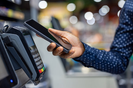 Person using a mobile phone to make a contactless payment at a point of sale terminal in a retail...