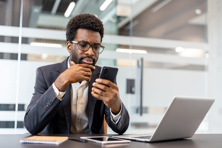 Thoughtful businessman finding solution, concentrating on mobile communications in a modern office setup, embracing strategy and efficiency during his daily workflowの写真素材