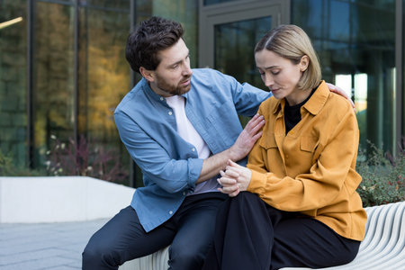 Man supporting a sad woman with a comforting hand on her shoulder while sitting together on an...