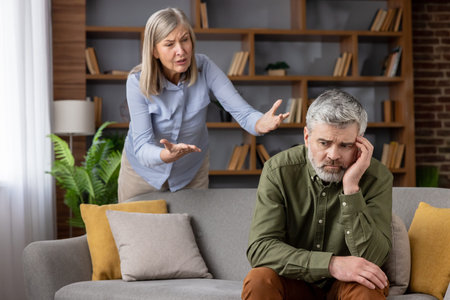 Angry mature woman arguing with sad man experiencing stress and communication problems during a difficult marriage dispute or family problem on a sofaの写真素材