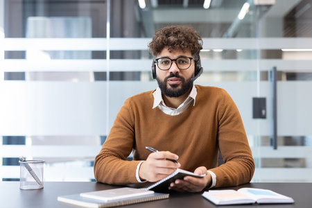 Young man wearing a headset and glasses, actively participating in a video conference from his...